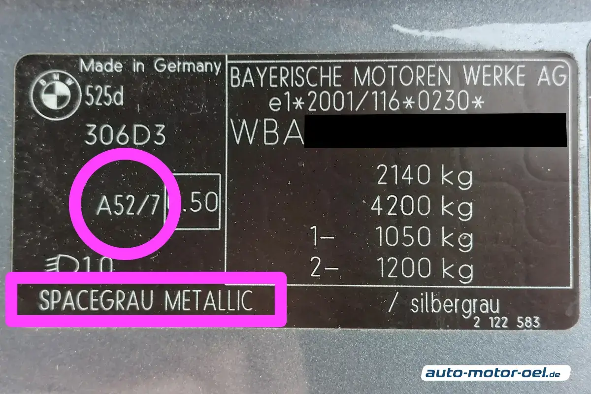 Der Farbcode ist die Zahl vor dem Schrägstrich: Eine Nahaufnahme eines schwarzen BMW-Typenschilds auf einer grau-blauen Metalloberfläche. Auf der linken Seite ist der Code "A52/7" mit einem pinkfarbenen Kreis markiert. Am unteren linken Rand ist die Farbbezeichnung "SPACEGRAU METALLIC" mit einem pinkfarbenen Rechteck hervorgehoben. Das Schild enthält zudem technische Details wie das Modell „525d“, Gewichtsangaben in kg und das BMW-Logo. Die Beleuchtung ist helles Tageslicht mit leichten Reflexionen auf der Plakette.
